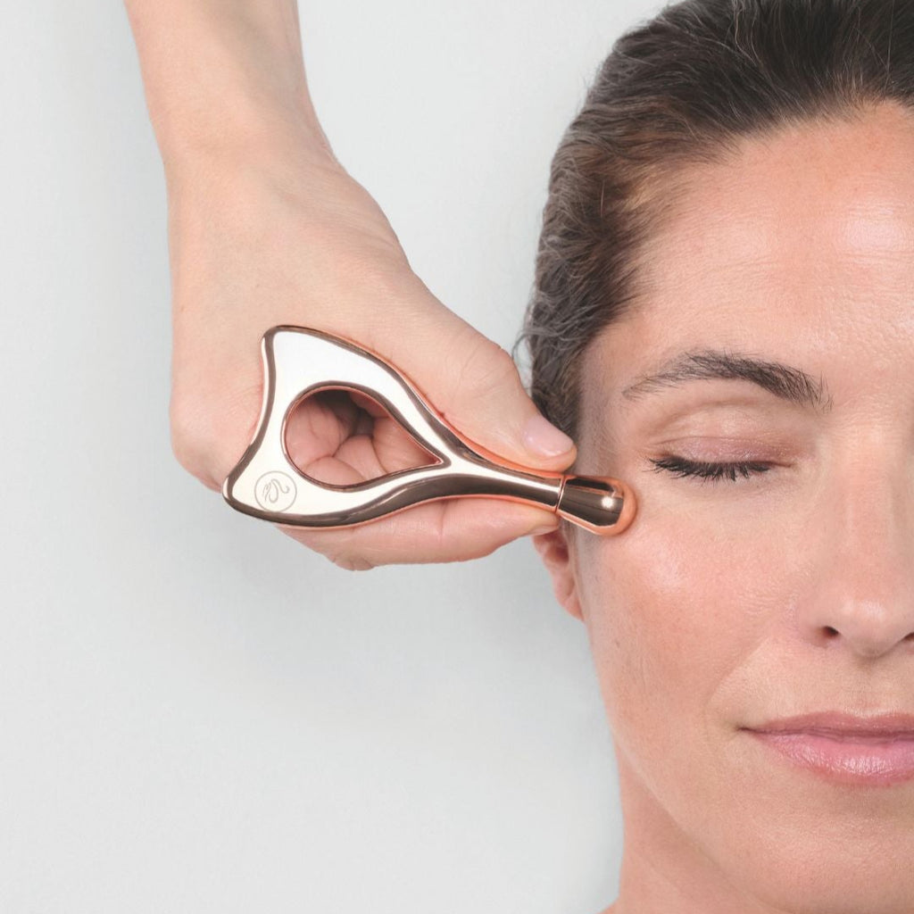 Person using a facial roller on another person's face against a white background