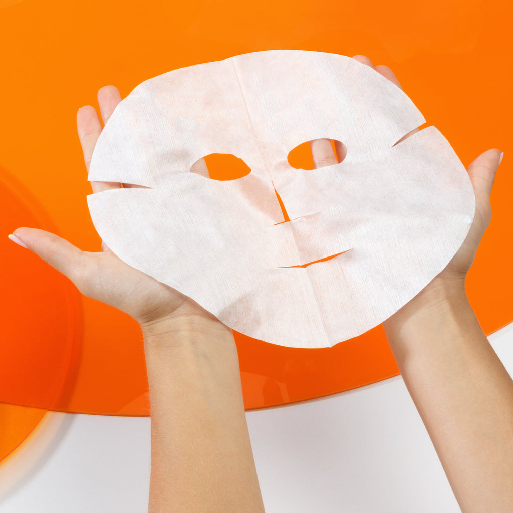 White vitamin c face mask held by hands against an orange background