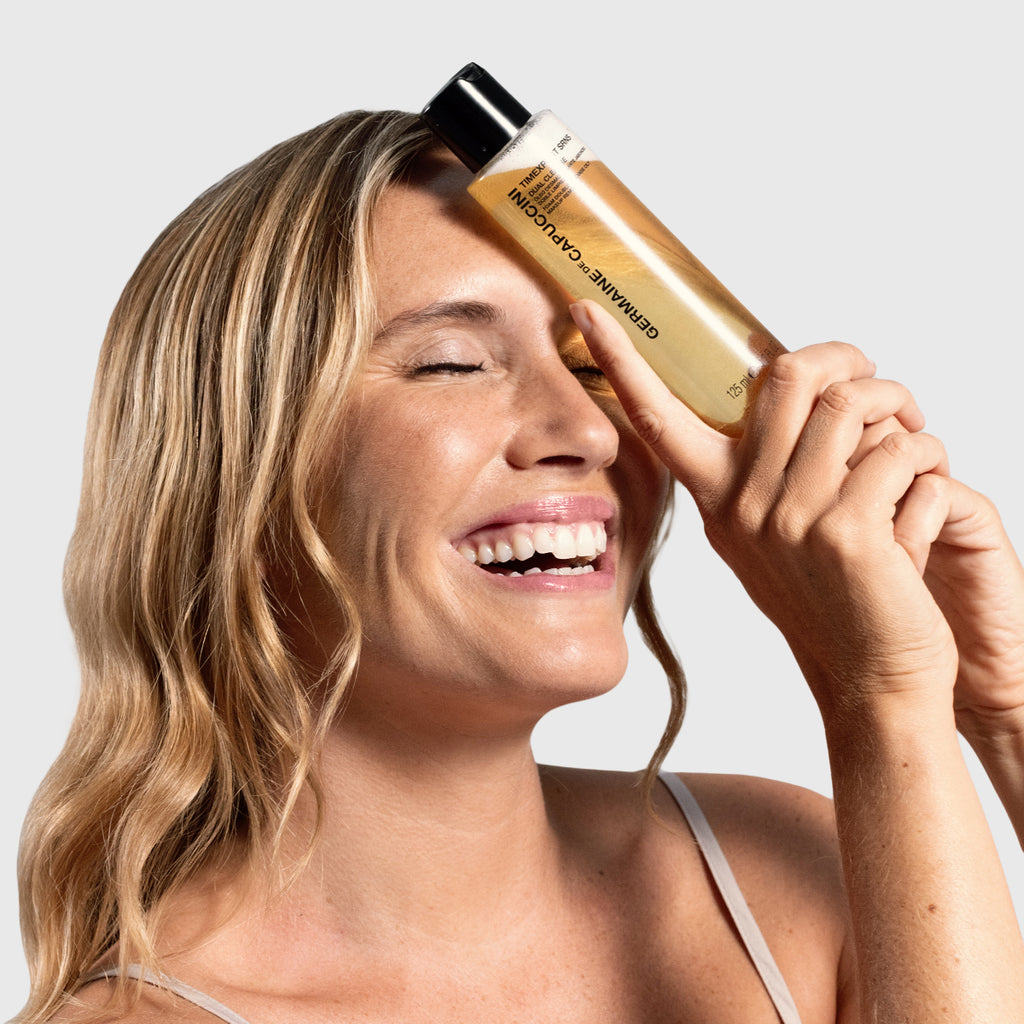 Woman with a dual cleanser product to her face with a neutral background