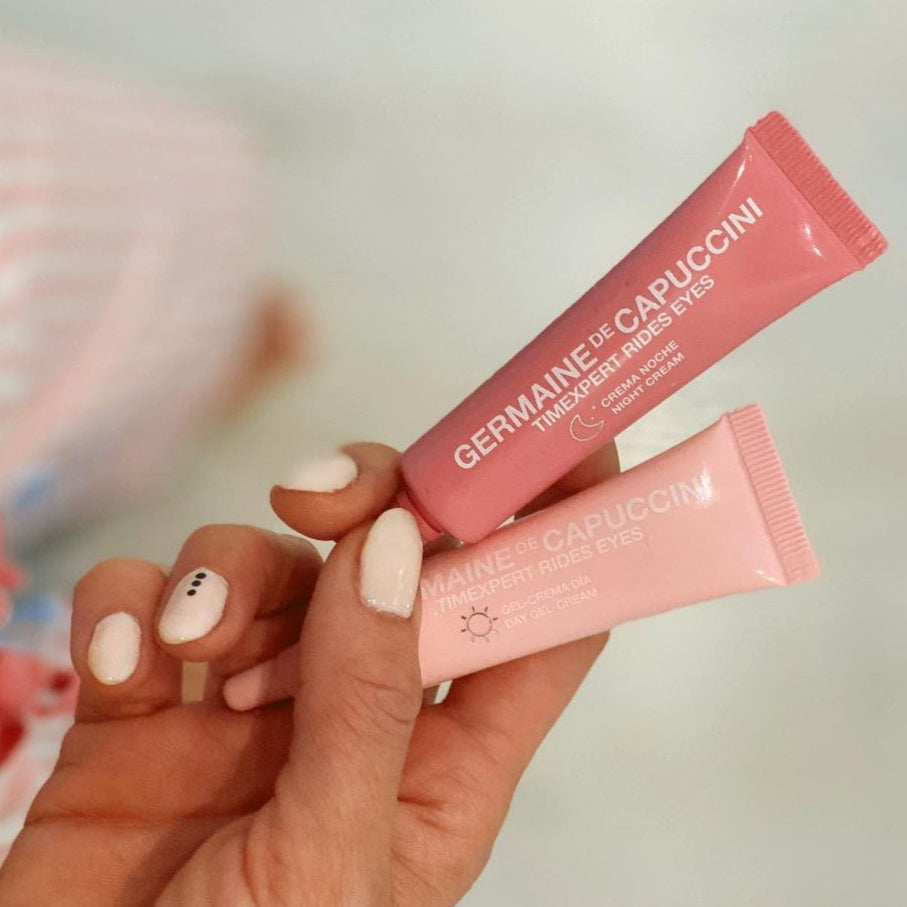 Two pink eye cream tubes held by a hand with a blurred background