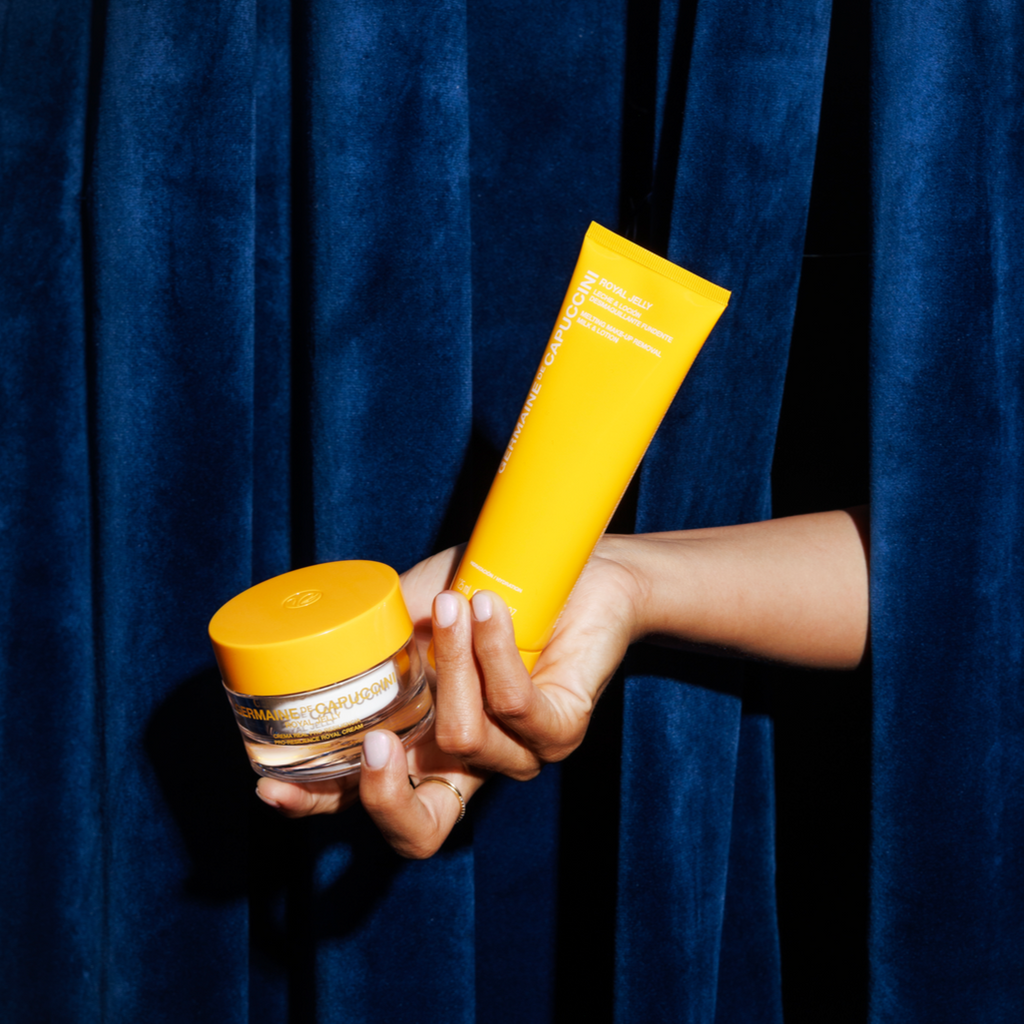 Hand holding two yellow skincare products against a dark blue curtain